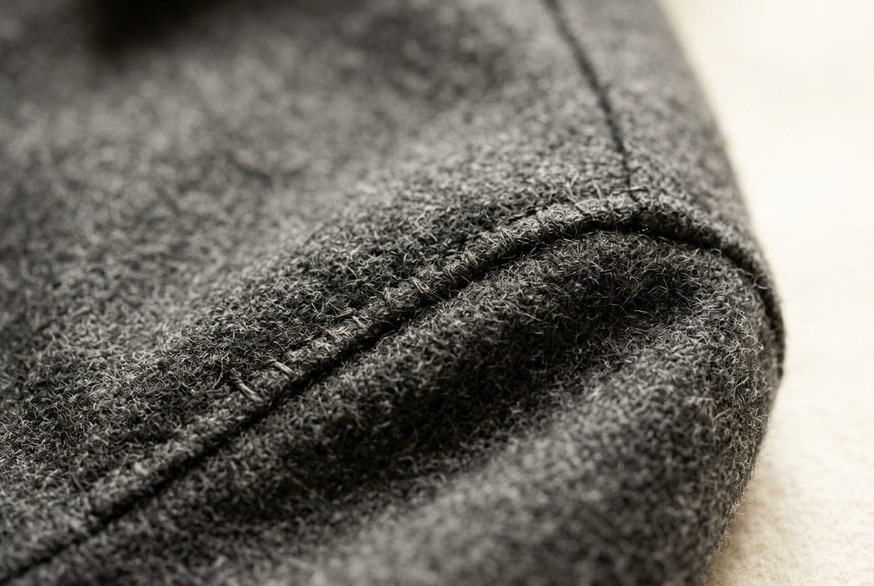 A macro of a charcoal wool coat shoulder, the sleevehead seam running over the shoulder line above the canvas roll