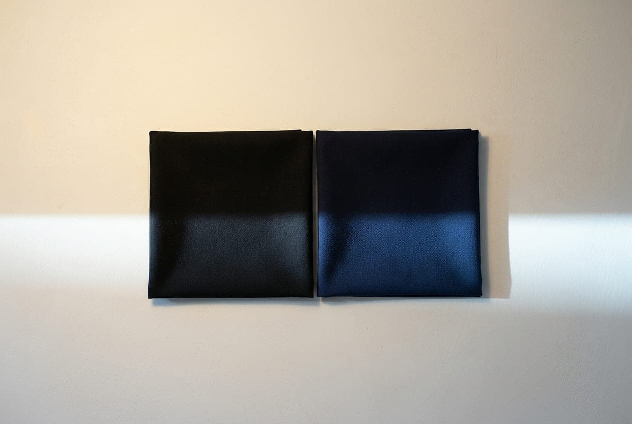 A black and a navy cloth side by side, each half lamplit and half daylit — indistinguishable in the warm upper half, clearly different in the cool lower half