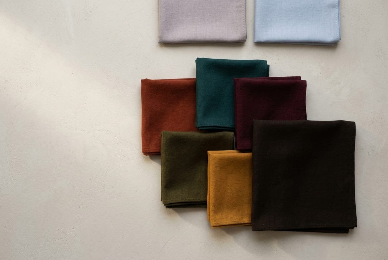Deep brick, dark teal and wine cloths over a near-black brown, with two pale dusty squares set apart