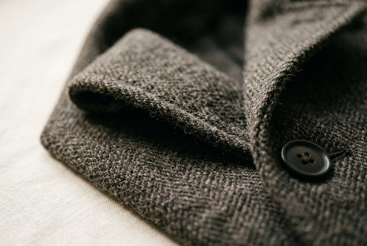 A macro of a wool coat front, the lapel rolling away above a flat buttoned overlap