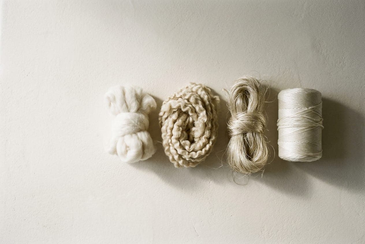 Four bundles of raw yarn — cotton, wool, a lustrous plant fibre and a synthetic filament