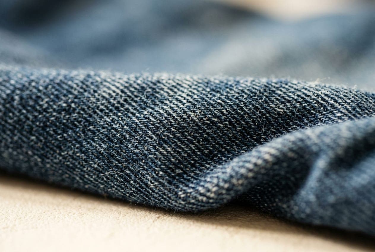 A macro of indigo denim showing the diagonal twill line and a relaxed fold