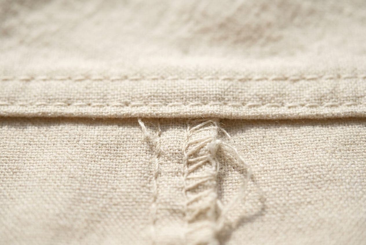 A macro of an evenly stitched seam above a puckered one in the same cloth