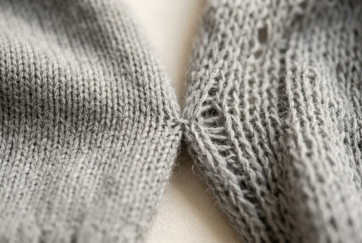 A macro of a dense fine-gauge knit meeting a loose uneven one in the same grey