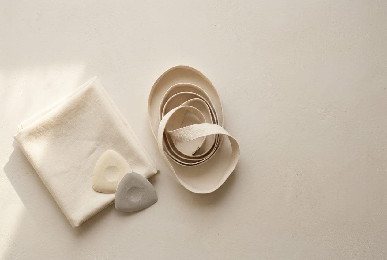 A blank cloth tape measure coiled beside a folded square of cream cloth